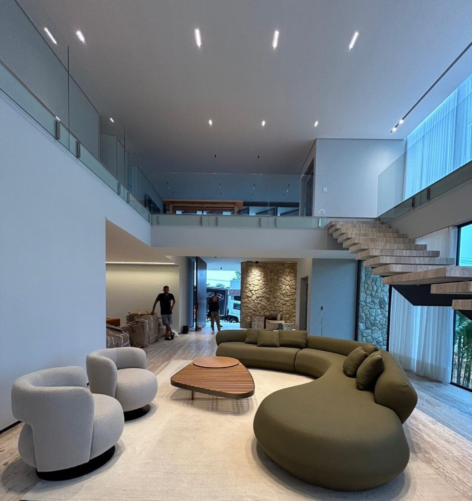 Sala com pé-direito duplo, escada de madeira e piso inteiro em travertino levigado