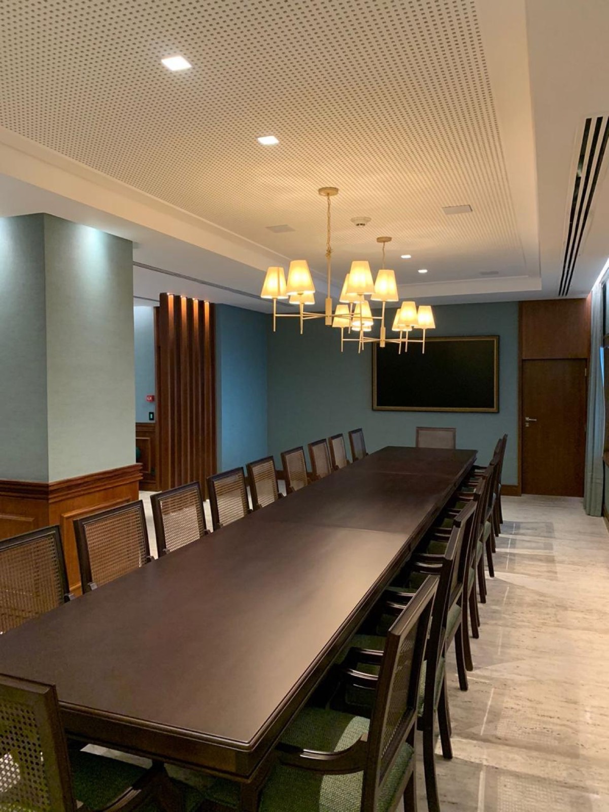 Salão de refeições com mesa longa, lustres e piso em travertino levigado